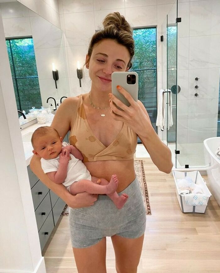 Woman taking a mirror selfie holding a baby in a bathroom setting, showcasing real-life moments.