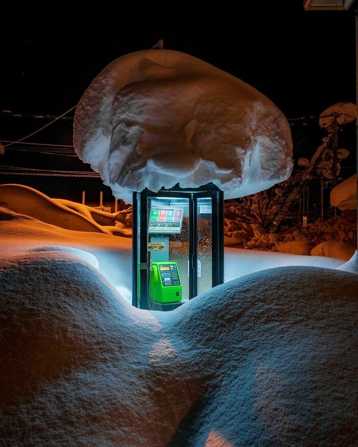 Phone booth covered in snow during winter night, showcasing ice-cold conditions.