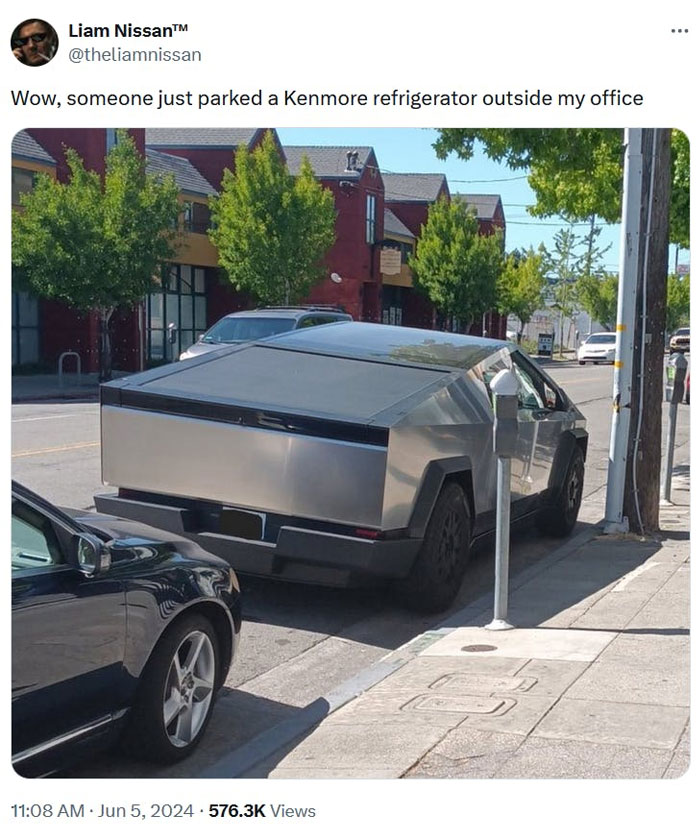 An E meme with a futuristic electric vehicle resembling an appliance, humorously compared to a refrigerator, parked on a city street.