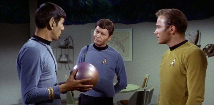  A famous trio from Star Trek, featuring Spock, Dr. McCoy, and Captain Kirk in conversation, with Spock holding a spherical object inside a futuristic setting.