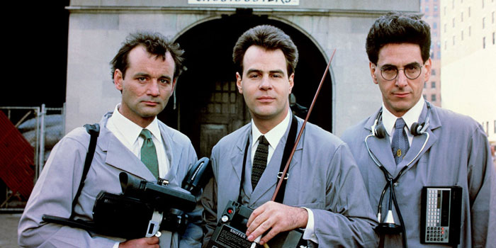 A famous trio from Ghostbusters, featuring Peter Venkman, Ray Stantz, and Egon Spengler in their ghost-hunting gear, standing together outside a building.