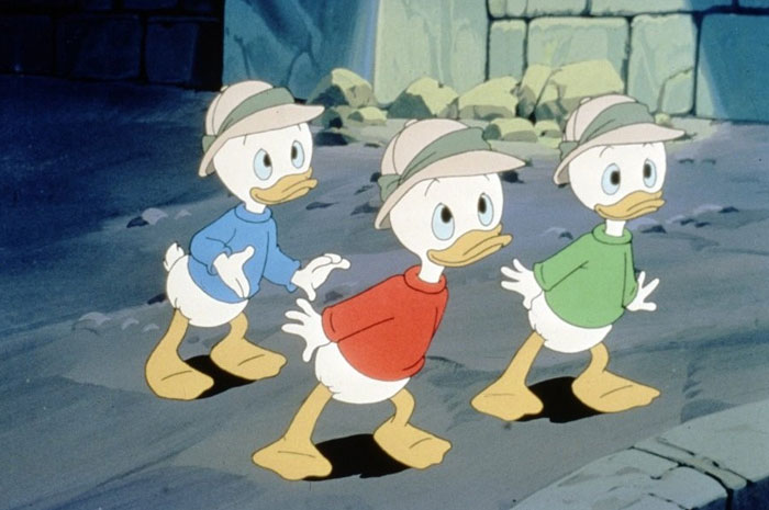 A famous trio from DuckTales, featuring Huey, Dewey, and Louie dressed in blue, red, and green shirts with explorer hats, standing in an adventurous setting.