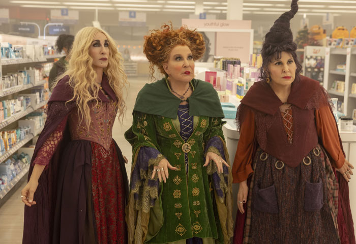 A famous trio from Hocus Pocus, featuring the Sanderson sisters—Sarah, Winifred, and Mary—in their witch costumes, standing inside a modern store.