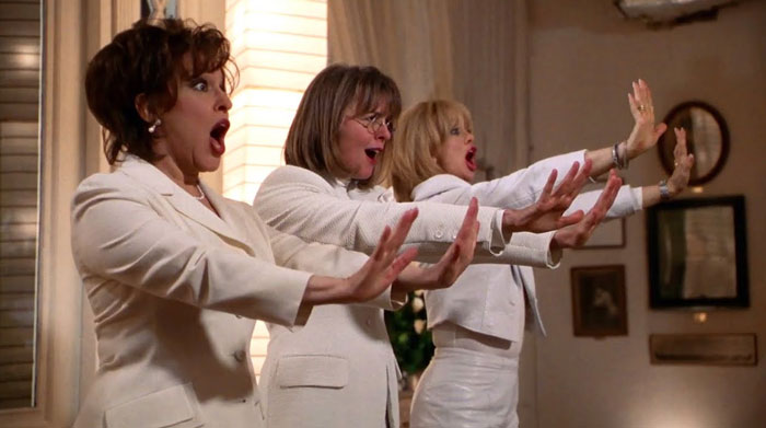 A famous trio from The First Wives Club, featuring Bette Midler, Diane Keaton, and Goldie Hawn dressed in white outfits, striking a dramatic pose with outstretched arms.