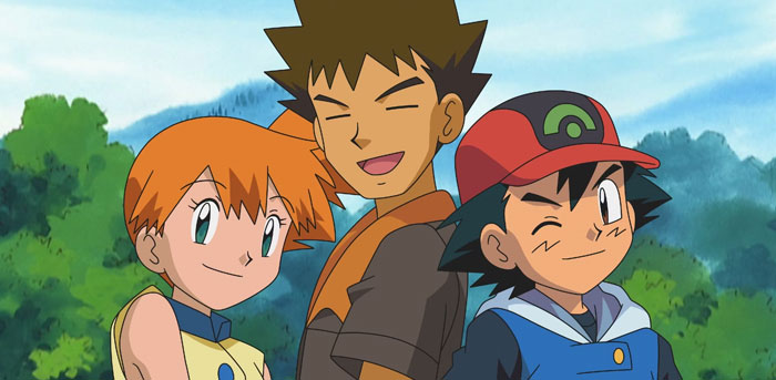 A famous trio from an anime series featuring Misty, Brock, and Ash standing together outdoors, with Ash winking and smiling.