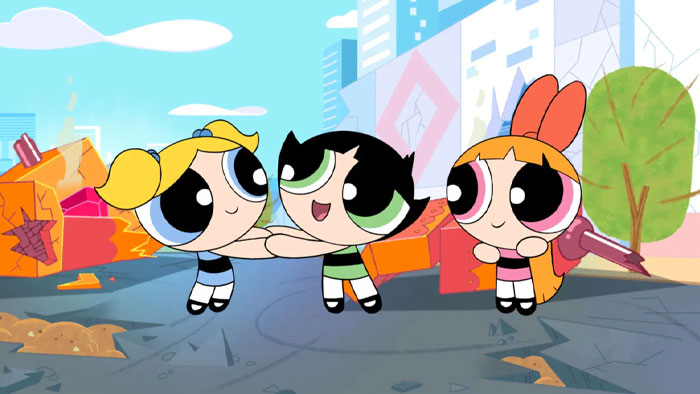 A famous trio from an animated series, the Powerpuff Girls, featuring Bubbles, Buttercup, and Blossom holding hands and smiling in a city scene.