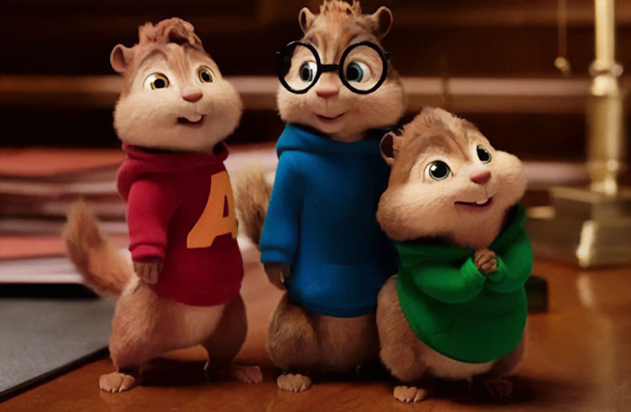 A famous trio from an animated series, Alvin and the Chipmunks, featuring Alvin in red, Simon in blue with glasses, and Theodore in green, standing together indoors.