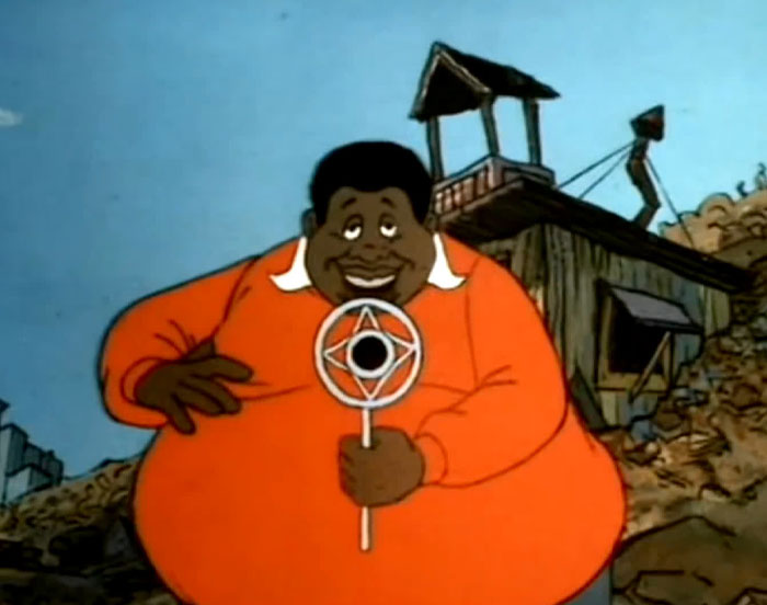 A fat cartoon character, Fat Albert, wearing a red sweater and holding a microphone, smiles while standing in a junkyard setting with a wooden structure in the background.