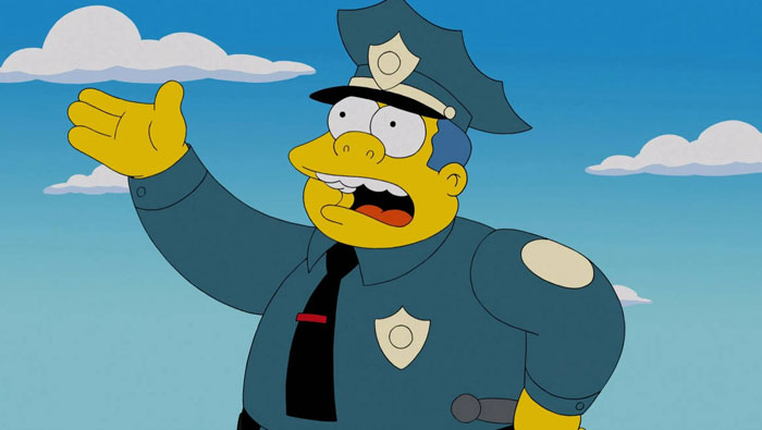 A fat cartoon character, Chief Wiggum, wearing a police uniform with a badge and hat, gestures with one hand while speaking against a blue sky with clouds.