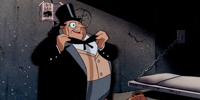 A fat cartoon character, The Penguin, wearing a tuxedo and top hat, adjusts his bow tie while standing in a dimly lit jail cell with chains and a cot.