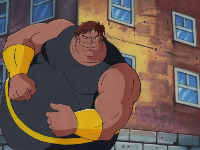 A fat cartoon character, the Juggernaut, with a muscular build, clenches his fists and smirks while standing in front of a building with worn walls and windows.