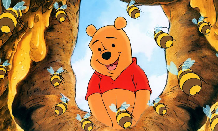 A fat cartoon character, Winnie the Pooh, wearing a red shirt, smiles while surrounded by buzzing bees inside a hollow tree with honey dripping.