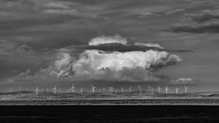 Black and white photo of wind turbines under dramatic clouds, showcasing breathtaking sustainability photography.