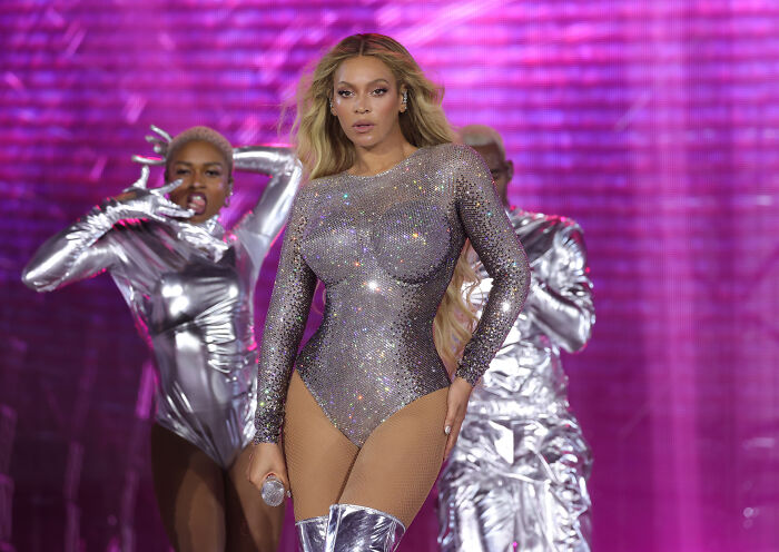 Popstar Beyoncé performs in a dazzling silver outfit with vibrant pink background and backup dancers.