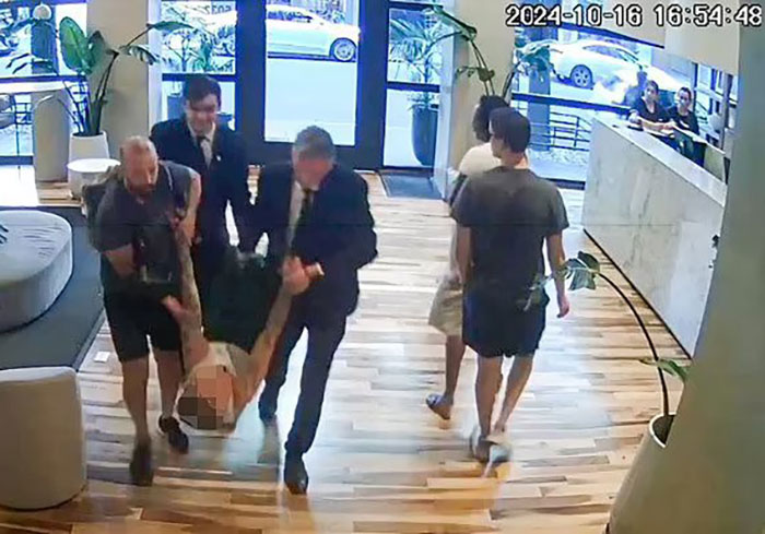 Security footage showing a group of people carrying someone in a hotel lobby.