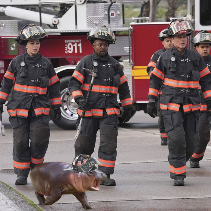 A Moo Deng meme featuring a baby hippo wearing a firefighter helmet, walking alongside firefighters in full gear in front of a fire truck.