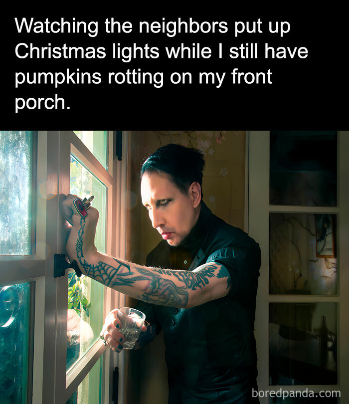 Tattooed person looks outside with a drink, capturing the essence of November's cringe-worthy memes and holiday contrast.