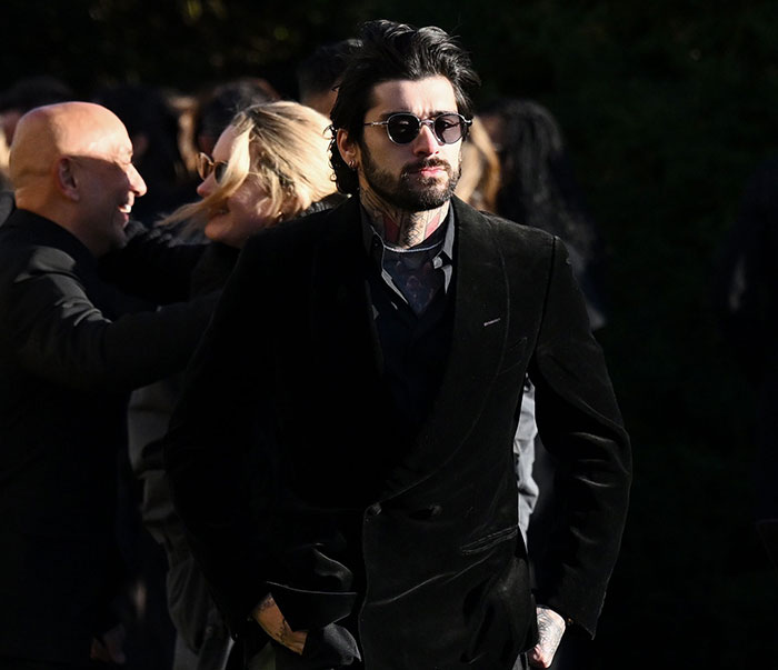 Man in a dark suit and sunglasses at an outdoor event, surrounded by people.