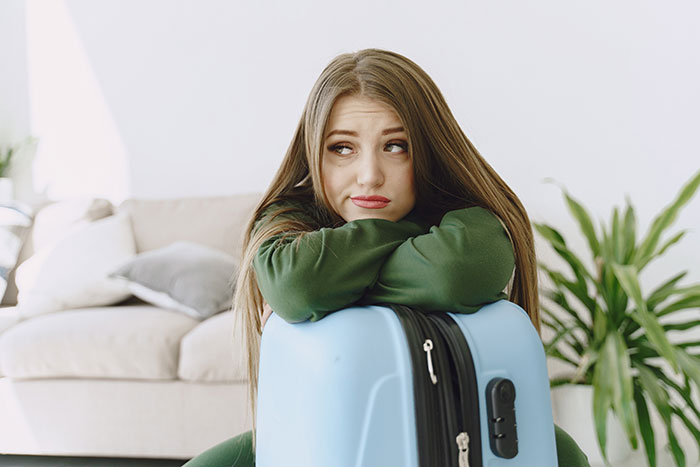 Passenger looking distressed, leaning on a blue suitcase indoors after a train detour.