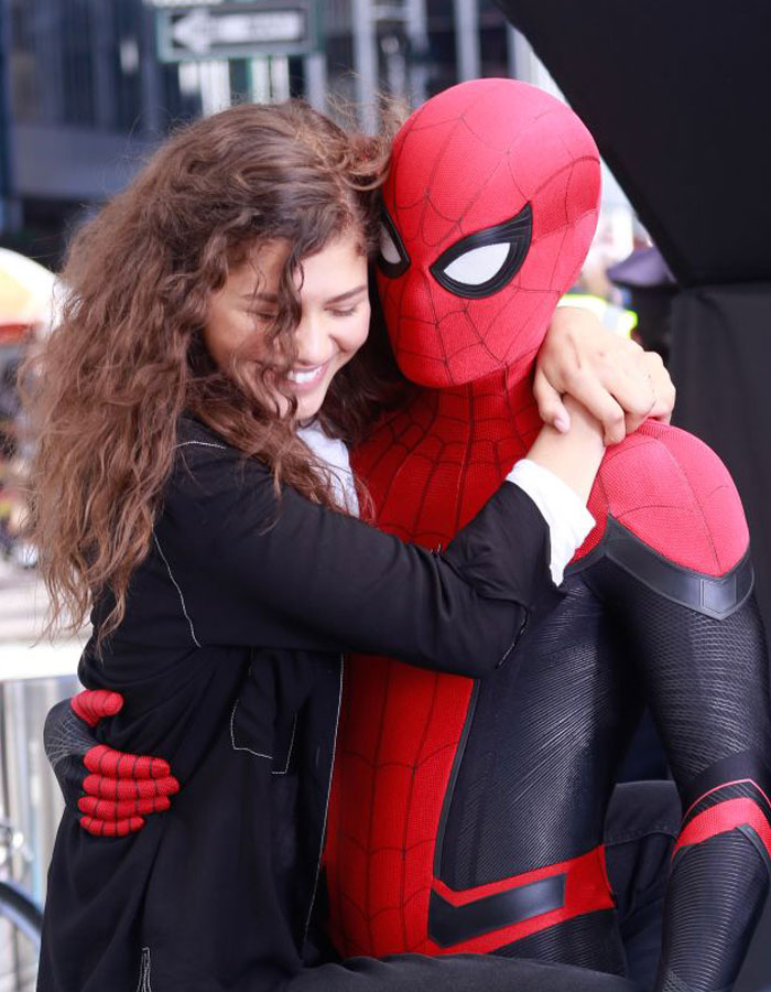 Zendaya hugging Spider-Man (in costume) on set, both smiling, showcasing a warm and playful moment during filming.