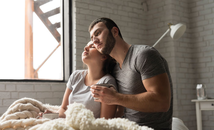 Couple relaxing in bed by a window, sharing a peaceful moment during the day.