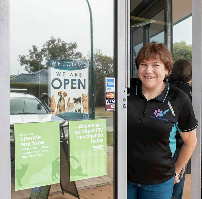 A woman stands at the entrance of a veterinary clinic promoting animal welfare, with signs about FIV vaccination.