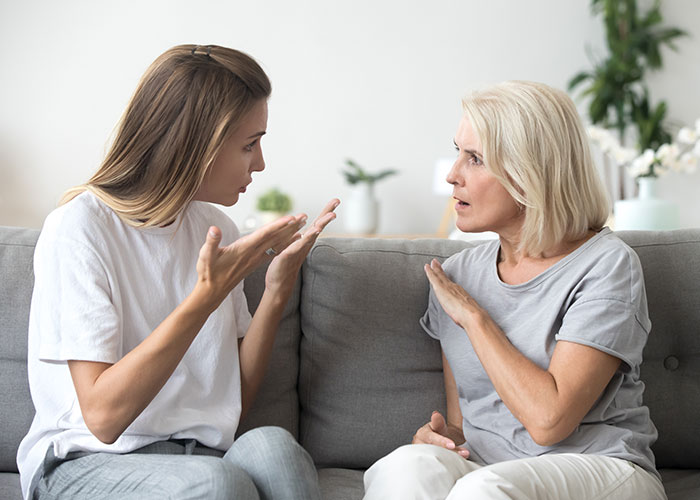 Two women sitting on a sofa, engaged in a heated discussion about family holidays.