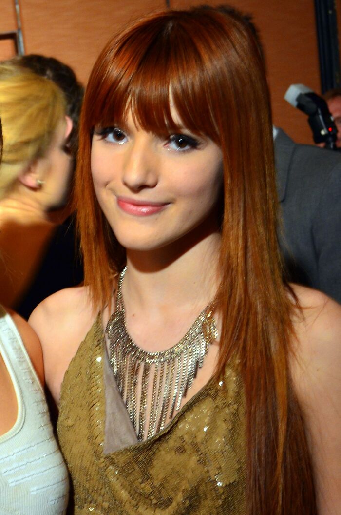 Young woman with long red hair and a gold dress, attending an event.