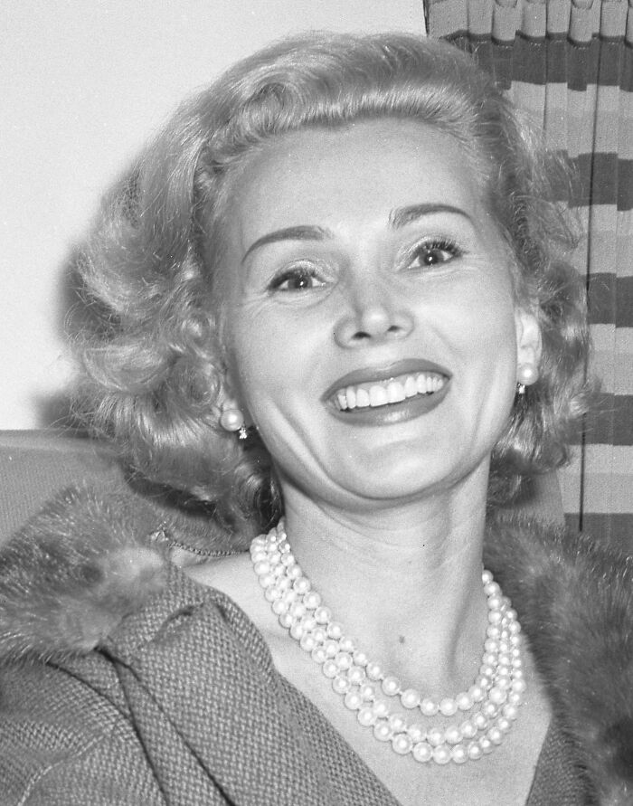 A smiling woman with short hair and pearl necklace, related to stories about celebrities.