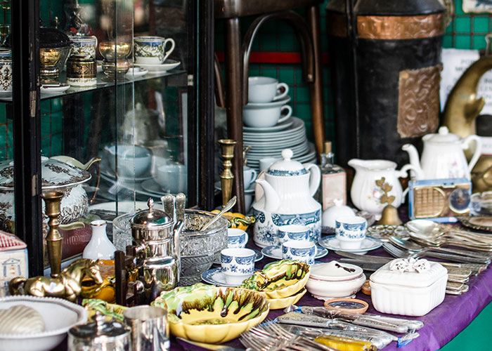 Antique tableware and silverware display, featuring vintage porcelain, teapots, and utensils arranged on a purple tablecloth.