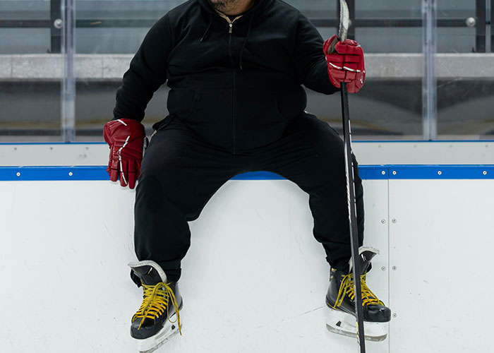 Person in hockey gear, holding a stick, sitting on a rink board, portraying a gut feeling of unease.