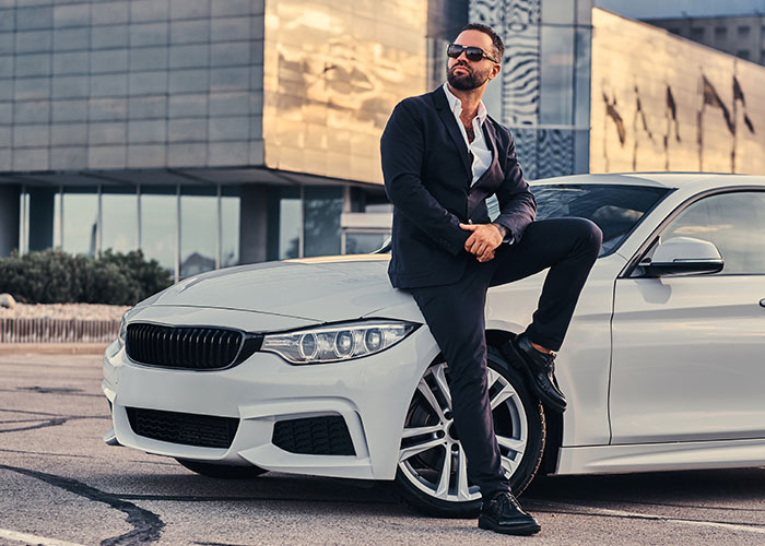 Man in a suit with sunglasses leaning on a white car, representing a confident gut feeling moment.