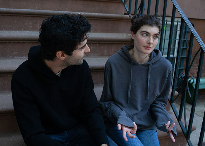 Two people sit on stairs, discussing gut feelings with intense expressions.