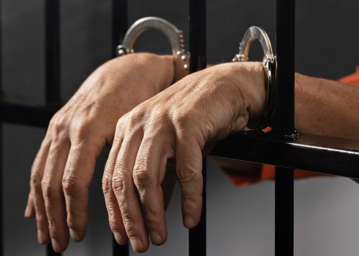 Hands in handcuffs gripping jail bars, illustrating unpleasant gut feelings being accurate.