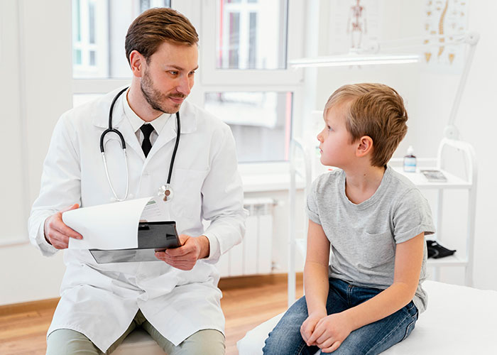 Doctor consulting a young boy in a medical office, both engaged in conversation about gut feelings.