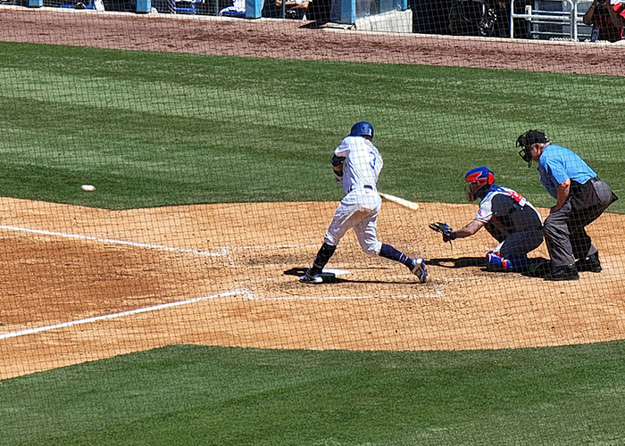 Baseball player swings at bat as umpire and catcher look on, capturing a moment where a gut feeling could be accurate.