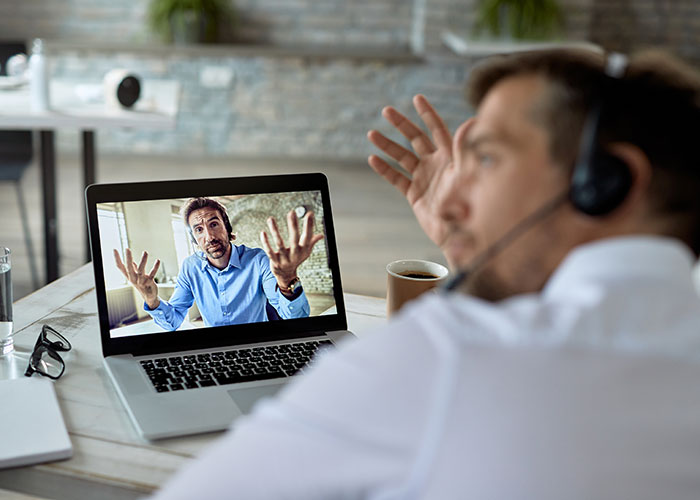 Man in virtual meeting, expressing concern, with another man wearing a headset, illustrating unpleasant gut feelings.