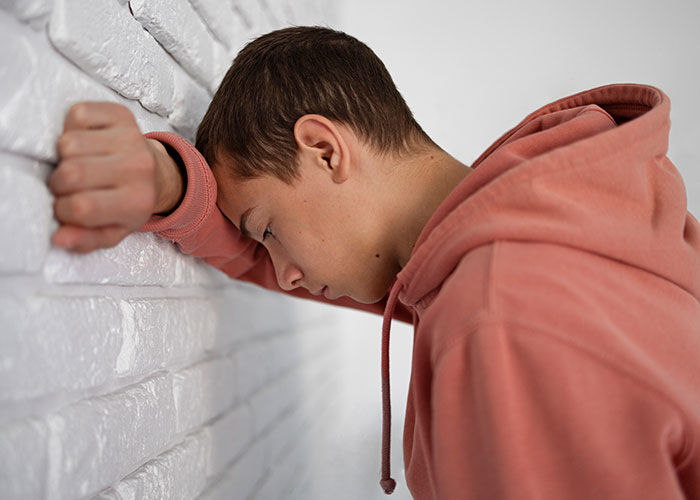 Person in a pink hoodie leaning against a white brick wall, conveying an unpleasant gut feeling.