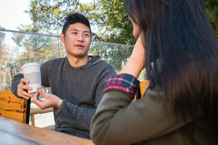 A man and woman in conversation outdoors, with the man holding a coffee cup, discussing Japanese culture.