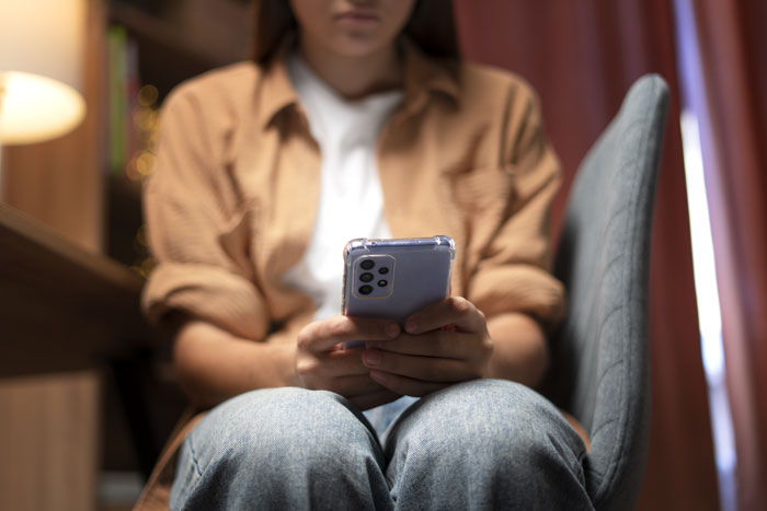 Woman sitting on chair holding phone, feeling uncomfortable in a room themed with Japanese culture.