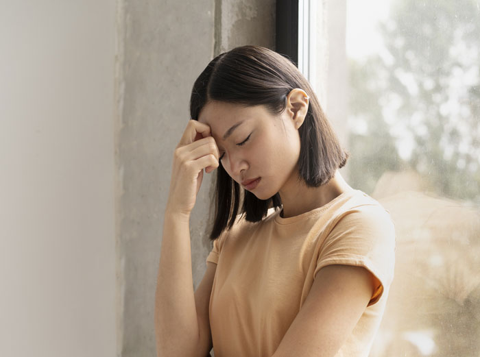 Woman looking stressed, leaning against a window, feeling uneasy about Japanese culture-themed decor.