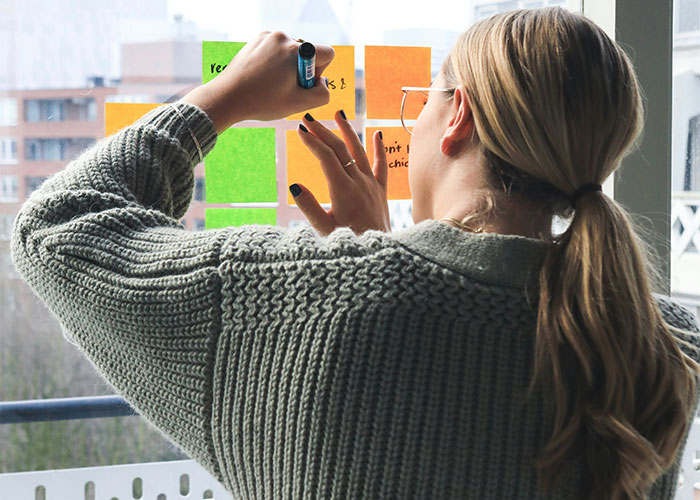 Woman planning her clever payback, writing notes on colorful sticky notes by a window.