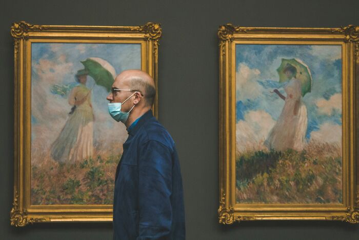 Man in a gallery with Monet paintings, hinting at wealth through art collection.