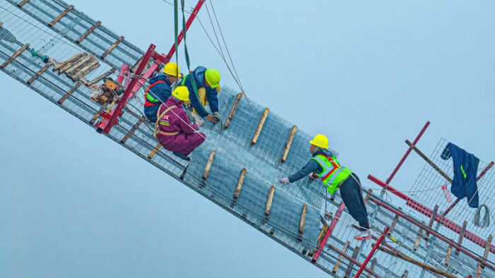 Workers in safety gear installing solar panels on a suspension bridge, showcasing sustainability in breathtaking photography.