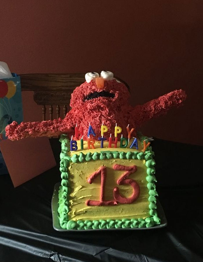 A birthday cake inspired by the Elmo fire meme, with an Elmo figure raising its arms atop a "Happy Birthday" sign and the number "13" on the cake.