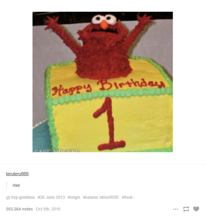 An Elmo fire meme-inspired cake with Elmo raising its arms on top of a birthday cake. Text on the cake reads “Happy Birthday” and “1,” with the caption “rise.”