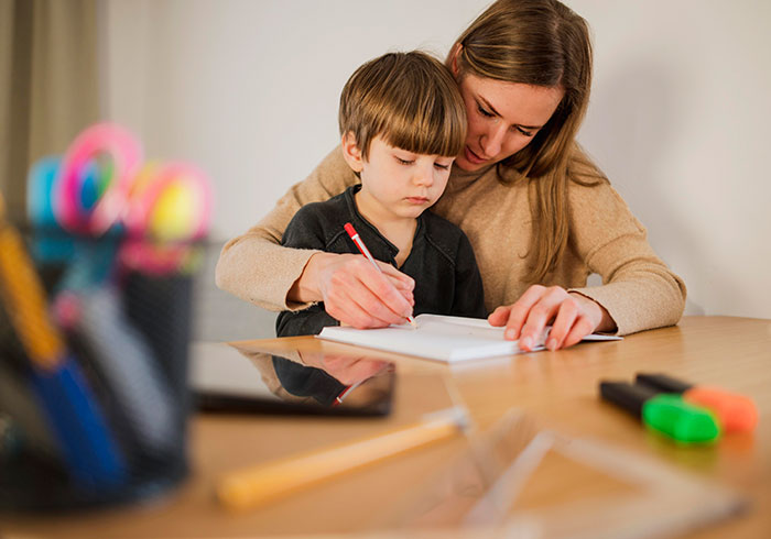 A young mother with her child, both focused on drawing at a wooden table, depicting early parenting challenges.