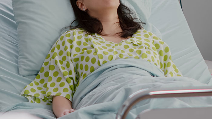 Teen girl in hospital bed feeling awkward, wearing a polka dot gown, discussing challenges of having a baby young.