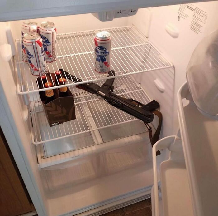 Open fridge with beer cans, bottles, and an unloaded rifle; an example of a chaotic dude fridge.