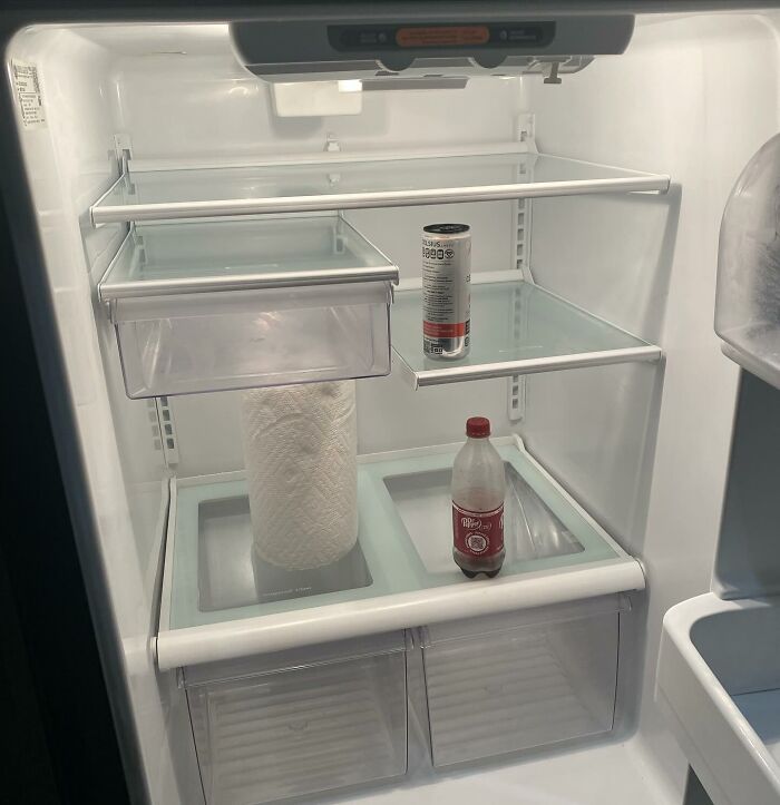 Sparse contents in an open 'dude fridge' with Dr Pepper, energy drink, and paper towel roll.